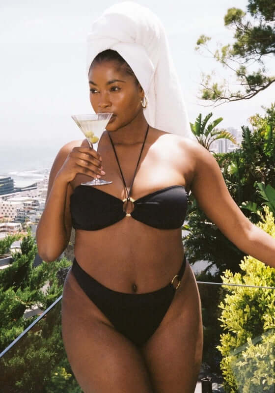 Acapulco Bikini Black by Away That Day, model wearing black bandeau bikini with ring detail, holding a martini.