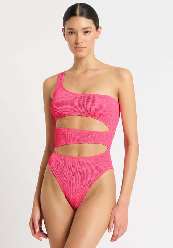 Rico Swimsuit Azalea in hot pink with slashed cut outs, one shoulder neckline, and high hip cut, showcasing stylish beachwear.