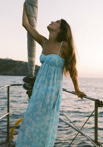 Everlasting Maxi Dress Paper Daisy by Peony, a woman in a flowing blue and white daisy print dress on a boat at sunset.