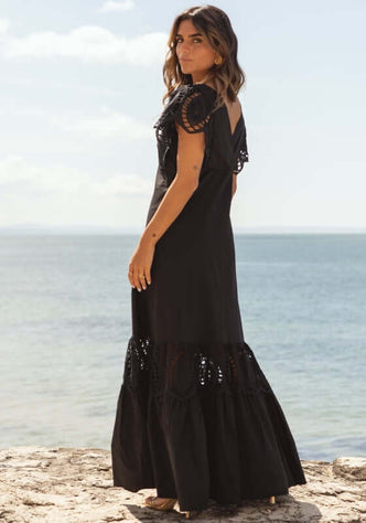 Copacabana Dress Black by Sole Lisboa, showing a model in a black maxi dress with peplum skirt and eyelet cutouts.