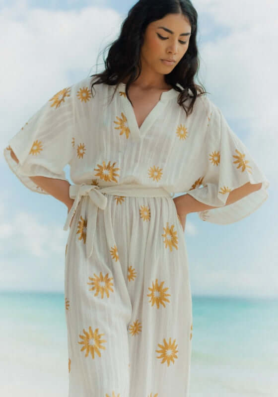 Dalhia Jumpsuit Coppacabana by Sundress, featuring a model in a slouchy white jumpsuit with gold sun motifs.