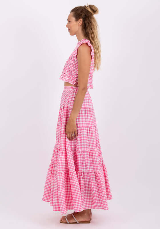 Odette Skirt Pink Gingham by Sundress, model wearing pink gingham tiered maxi skirt from side view.