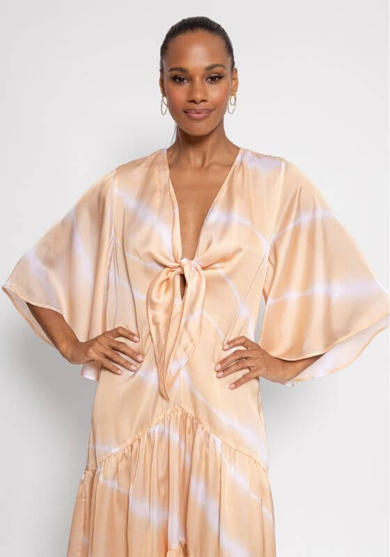 Anika Tie Dye Dress by Sundress model wearing flared white and beige tie dye dress with V-neckline tied in a knot.