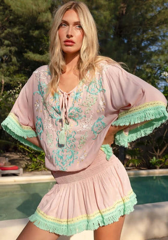 Sejla Kaftan Pink by Miss June, featuring pink fabric with turquoise embroidery and fringe details.