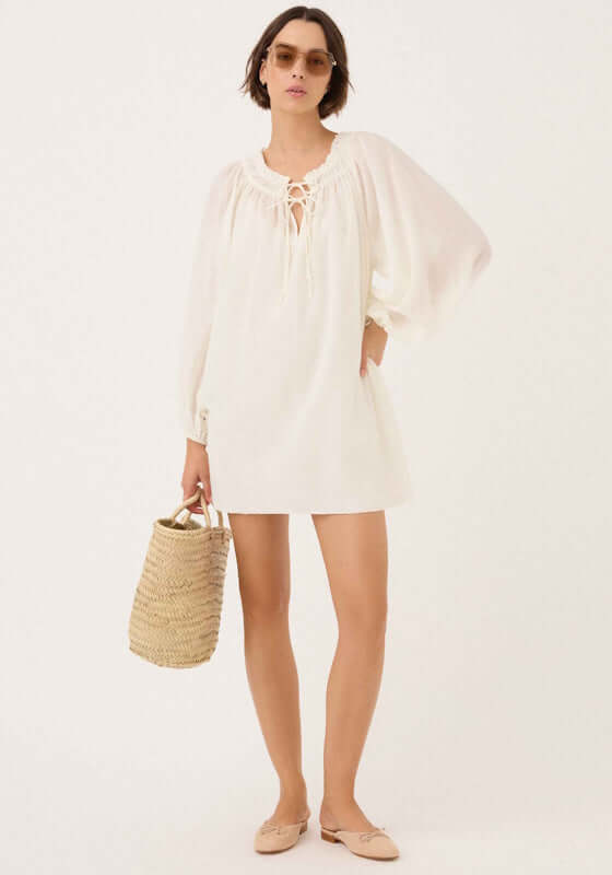 Audrey Mini Dress Gardenia by Peony, showcasing a model in a white mini dress with balloon sleeves and a woven bag.