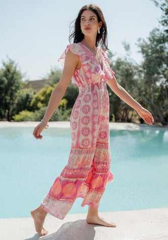 Sri Lanka Dress Pink by Piti Cuiti, a model in a pink floral dress by a pool showcasing its frilly V-neckline.