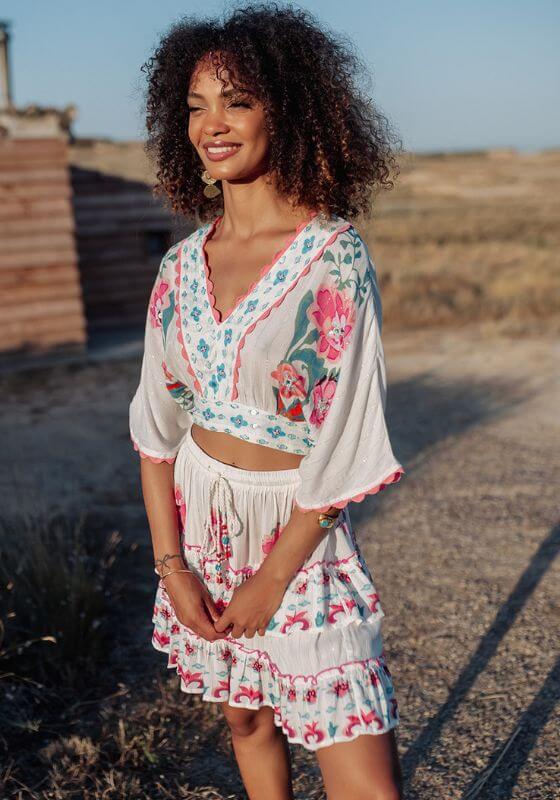 Bonaire Skirt White Pink by Piti Cuiti, model wearing vibrant tiered mini skirt with floral patterns, enjoying sunny day.