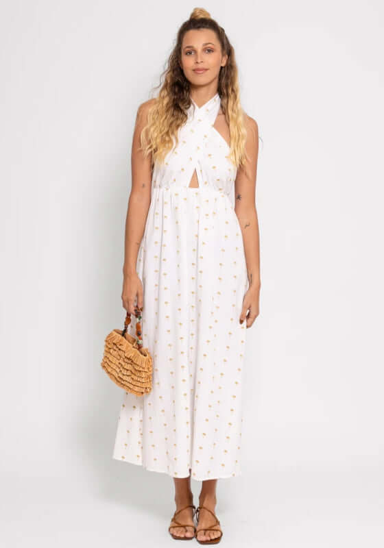 Aminy Dress by Sundress shows a backless white and gold maxi beach dress with palm tree embroidery and a leg slit.