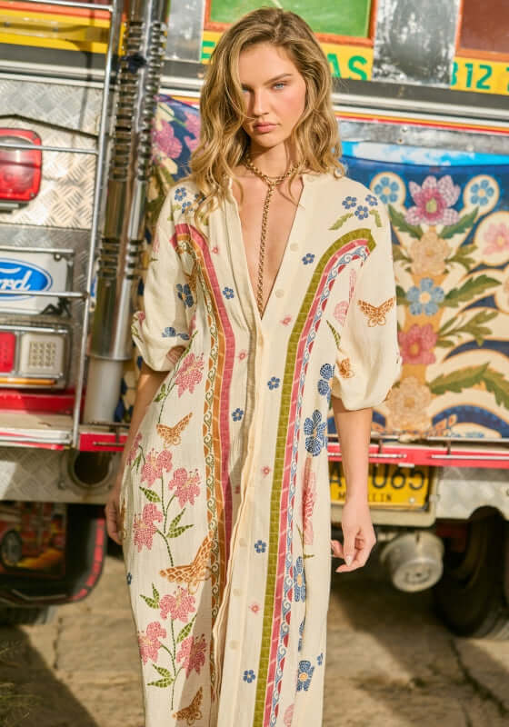 Clavelina Fiore Beach Tunic by Agua Bendita, a model in a maxi cover-up with floral print, standing by a colorful background.
