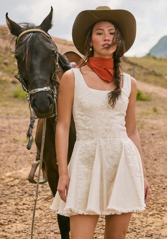 Kristen Sereia Dress by Agua Bendita, model wearing a mini dress with a pleated skirt beside a horse.