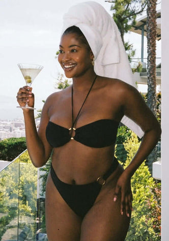 Acapulco Bikini Black by Away That Day, model wearing bandeau bikini with ring detail, holding martini.