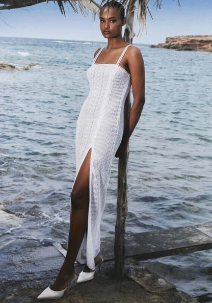 Vannie Long Dress White by Charo Ruiz, model wearing a stylish white dress with side slit by the beach.