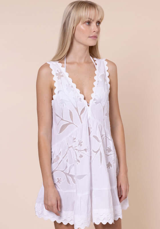 Floral Cutwork V Neck Mini Dress White by Juliet Dunn. Model wearing a white mini dress with floral cutwork and scalloped hem.
