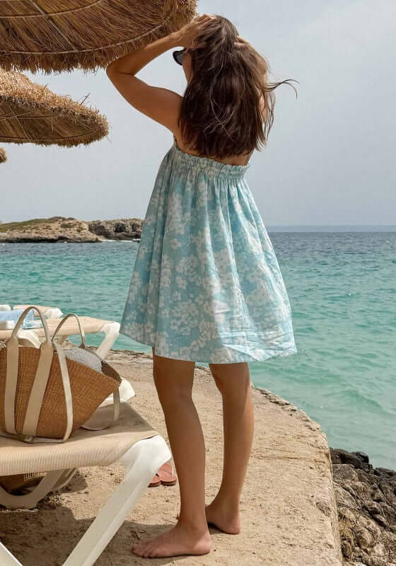 Ruched Mini Dress Paper Daisy by Peony, a girl in a blue and white floral dress at the beach, enjoying summer vibes.