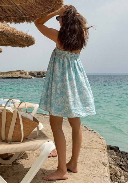 Ruched Mini Dress Paper Daisy by Peony, a girl in a blue and white floral dress at the beach, enjoying summer vibes.