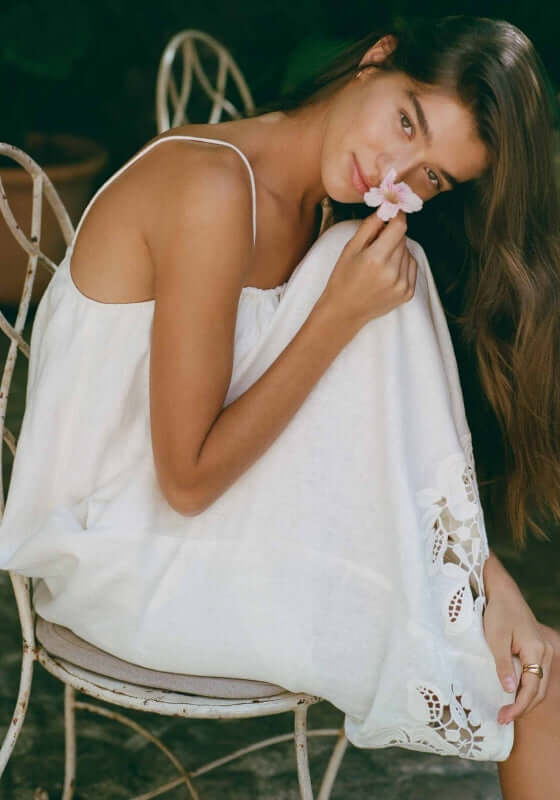 Embroidered Midi Dress Gardenia by Peony model poses with delicate flower, showcasing the dress's embroidery and relaxed fit.