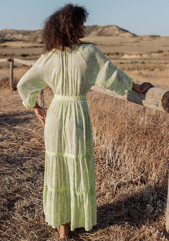 Sahara Long Dress Neon Green by Piti Cuiti, featuring a V-neckline and balloon sleeves against a serene outdoor backdrop.