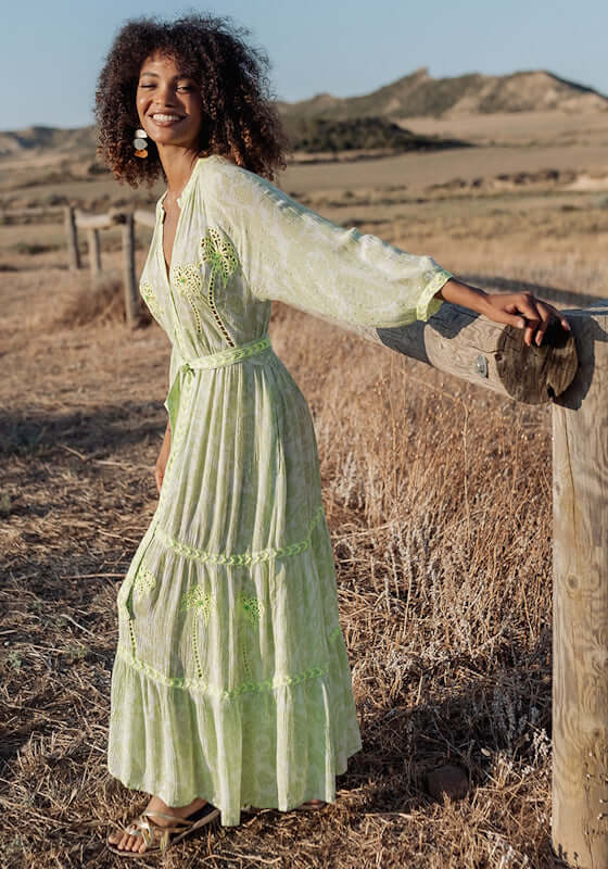 Sahara Long Dress Neon Green by Piti Cuiti, featuring a smiling model in a sunlit field wearing a long neon green maxi dress.
