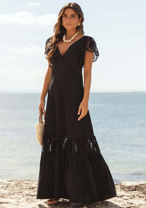 Copacabana Dress Black by Sole Lisboa, featuring V-neckline, peplum skirt, and eyelet cutout sleeves at the beach.