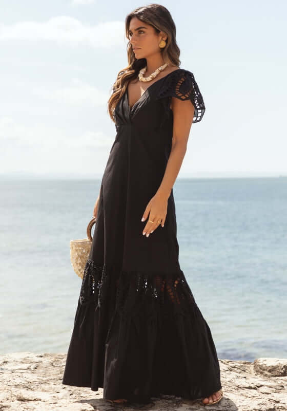 Copacabana Dress Black by Sole Lisboa, featuring a V-neckline and eyelet cutout details by the beach.