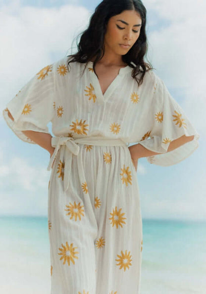 Dalhia Jumpsuit Coppacabana by Sundress, featuring a model in a slouchy white jumpsuit with gold sun motifs.