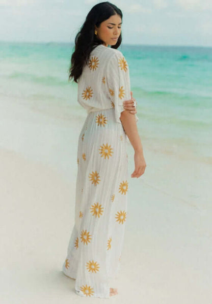 Dalhia Jumpsuit Coppacabana by Sundress worn by model on beach, featuring gold sun motifs and floaty sleeves.