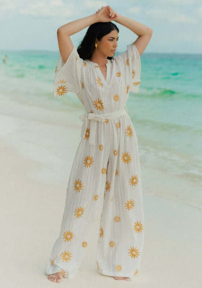 Dalhia Jumpsuit Coppacabana by Sundress, elegant white jumpsuit with gold sun motifs on a beach.