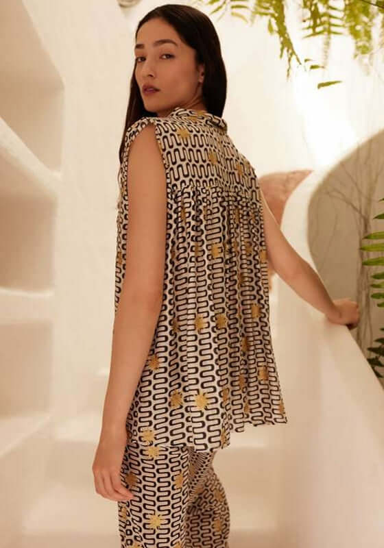 Assia Blouse Symi Black by Sundress, model wearing a stylish sleeveless black blouse with gold suns.