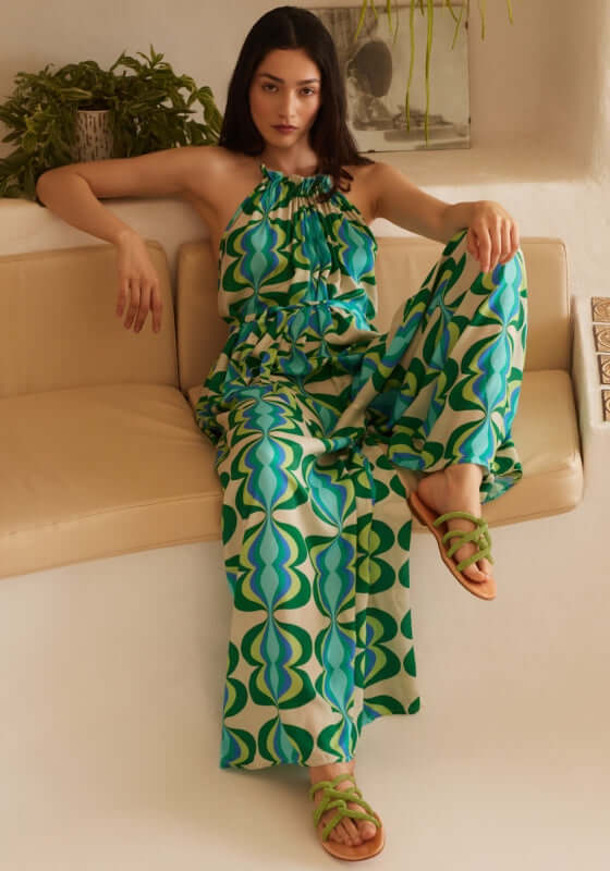 Sophie Jumpsuit Lullah by Sundress, featuring a model in a relaxed, green retro print jumpsuit sitting elegantly.