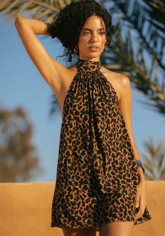 Ibiza Dress Leopard by Away That Day, model in a halter neck leopard print dress against a sunny backdrop.