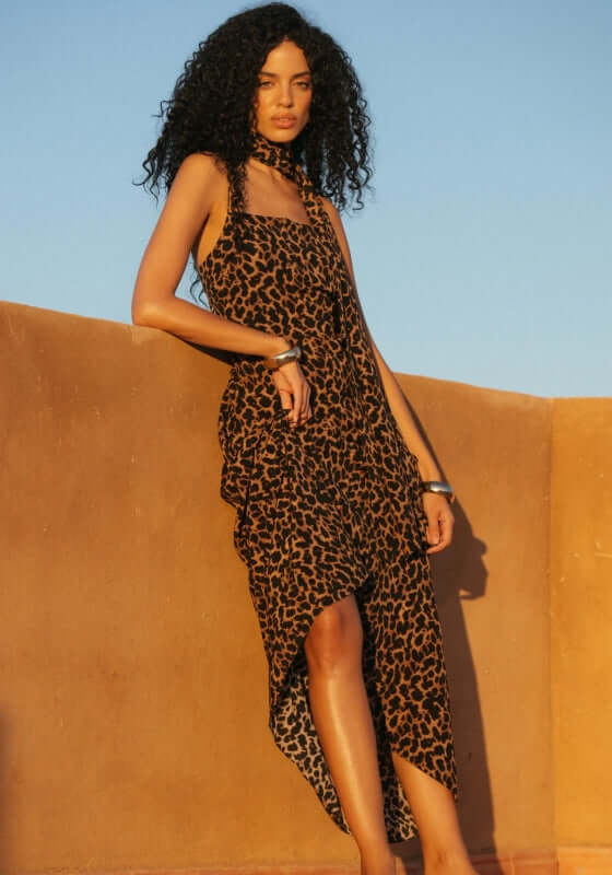 St Tropez Dress Leopard by Away That Day worn by a model against a sunset backdrop, showcasing its stylish design.