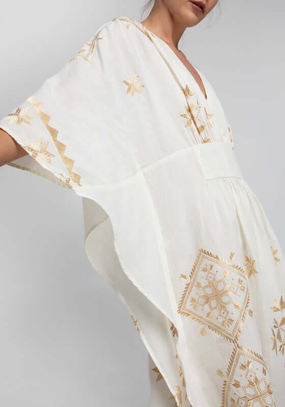 Lefkada Maxi V Neck Kaftan White by Greek Archaic Kori features a V-neck design and gold embroidery on flowing white fabric.