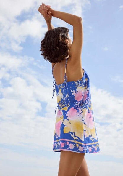 Floral Print Mini Dress Electric Blue by Juliet Dunn, featuring a model in a floral dress with tie spaghetti straps against a blue sky.