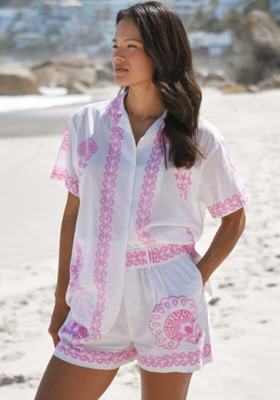 Calista Beach Shirt by Miss June, woman wearing white shirt with pink paisley print on beach, perfect for coastal style.