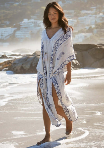 Gaya Kaftan by Miss June, model in flowy off-white kaftan with navy print, walking on the beach with slits for movement.