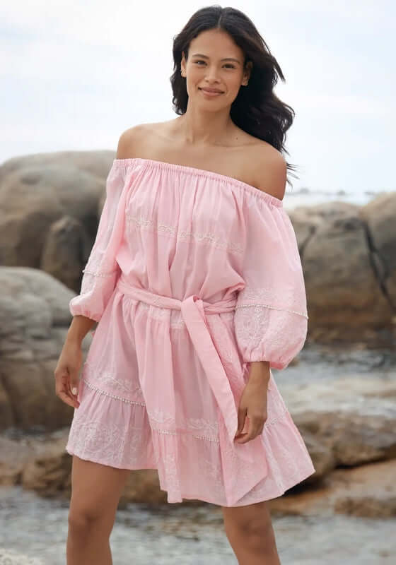 Layla Dress Pink by Miss June, model wearing soft pink off-shoulder dress with balloon sleeves on beach rocks.