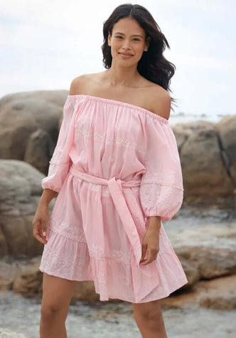 Layla Dress Pink by Miss June, model wearing soft pink off-shoulder dress with balloon sleeves on beach rocks.