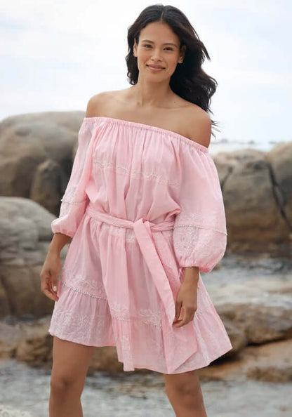 Layla Dress Pink by Miss June, model wearing soft pink off-shoulder dress with balloon sleeves on beach rocks.