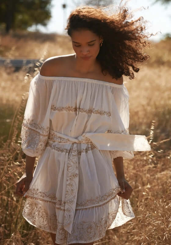 Layla Dress White by Miss June, model wearing an off-shoulder white dress with balloon sleeves and gold embroidery.