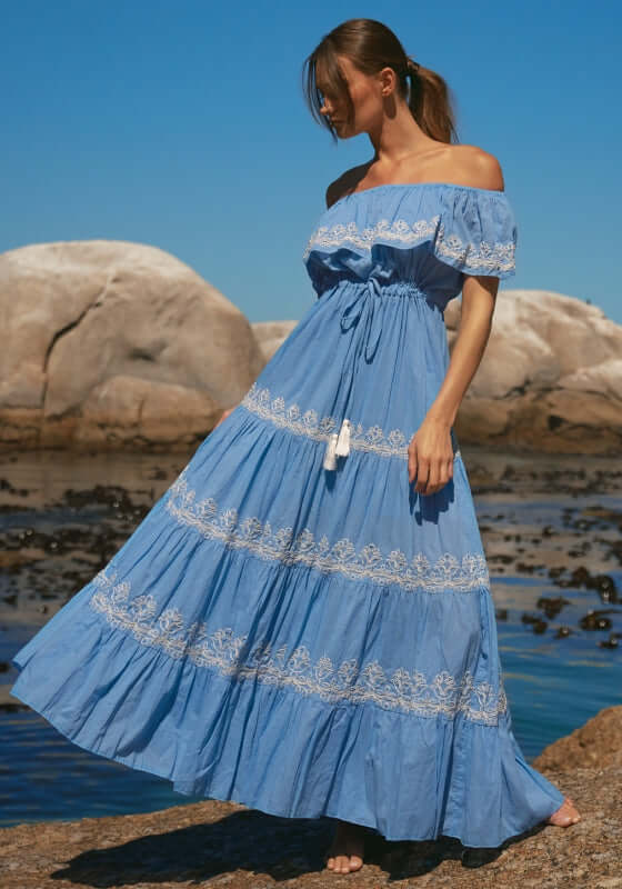 Malone Dress Blue by Miss June, showcasing a model in a blue maxi dress with off-shoulder neckline and white embroidery.