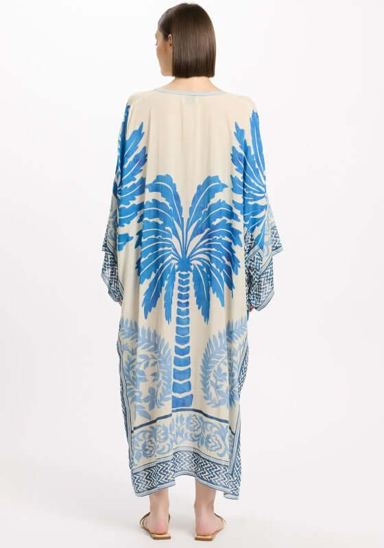 Rhoda Long Kaftan Blue by Miss June, showcasing a palm print in Mediterranean blue on a natural beige background.