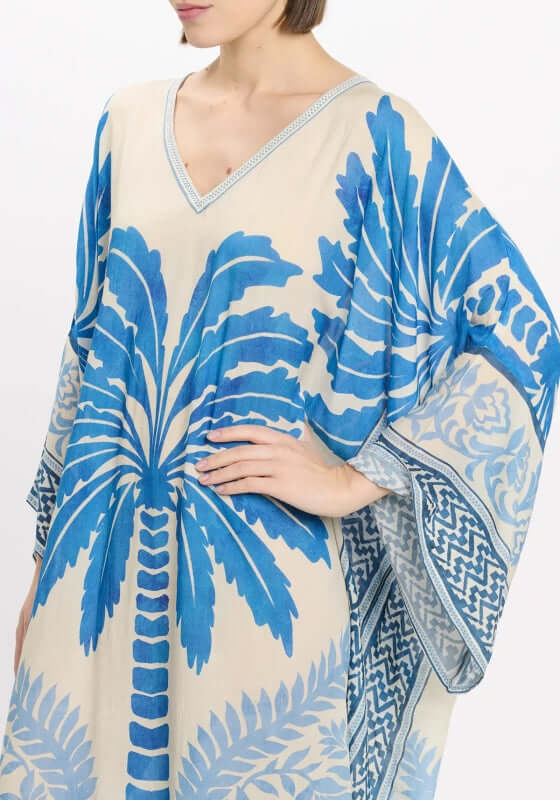 Rhoda Long Kaftan Blue by Miss June, featuring a tropical palm print in blue on beige fabric, flowing sleeves for elegance.