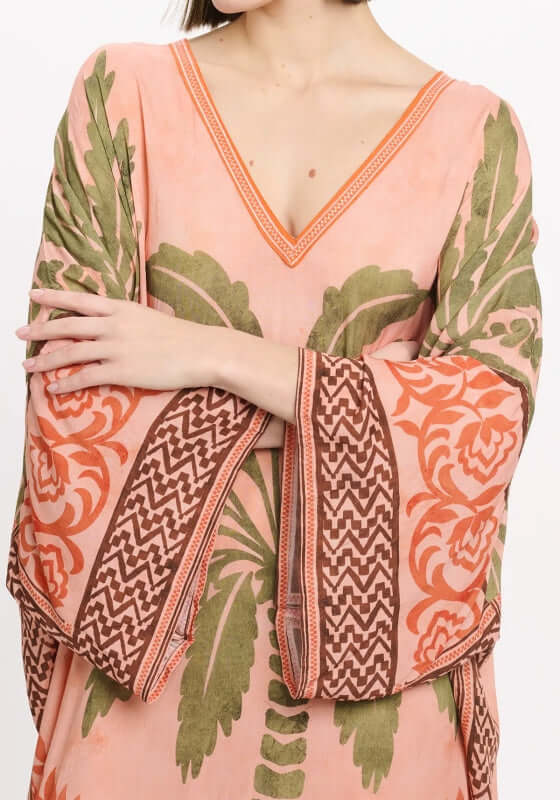 Rhoda Long Kaftan Peach by Miss June features a tropical palm print and flowing sleeves in a soft peach fabric.