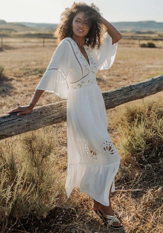 Barbados Dress White by Piti Cuiti, showcasing a woman in a flowy white maxi dress with peplum sleeves and embroidery.