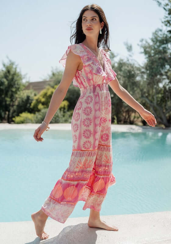 Sri Lanka Dress Pink by Piti Cuiti, a model in a pink floral dress by a pool showcasing its frilly V-neckline.