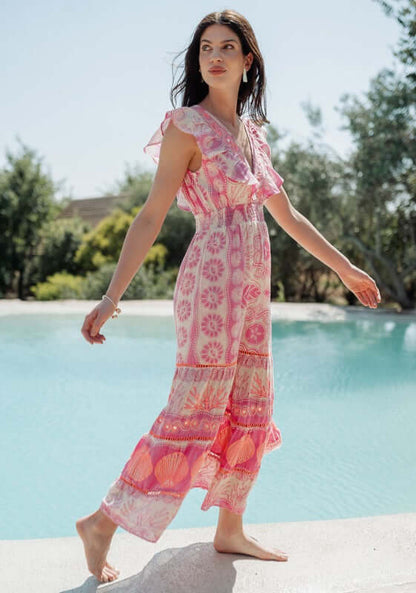 Sri Lanka Dress Pink by Piti Cuiti, a model in a pink floral dress by a pool showcasing its frilly V-neckline.