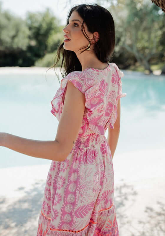 Sri Lanka Dress Pink by Piti Cuiti, featuring a woman in a pink dress with frilly neckline at a beach.