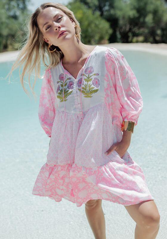 Amber Short Dress White Pink by Piti Cuiti, a woman in a floral-printed dress by a poolside, exuding effortless elegance.