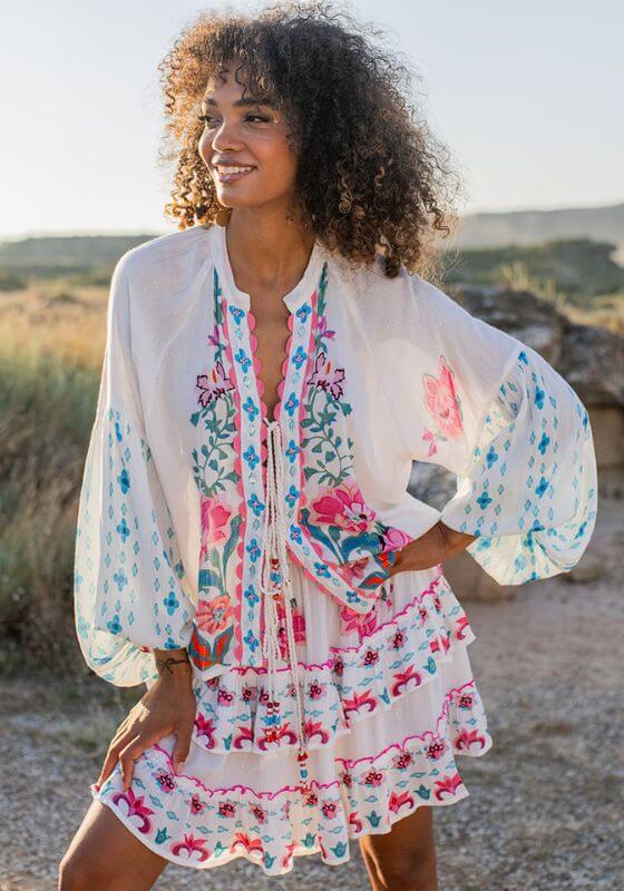 Bonaire Blouse White Pink by Piti Cuiti, featuring a tie-front closure and voluminous sleeves in a breezy beach scene.