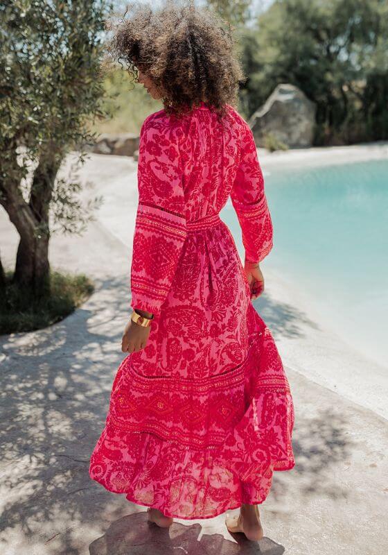 Samoa Dress Pink by Piti Cuiti, vibrant hot pink paisley print dress with flowing sleeves, tiered skirt, and belted waist.